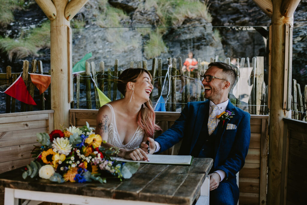 Bride and Groom laugh when signing the register at their beach wedding