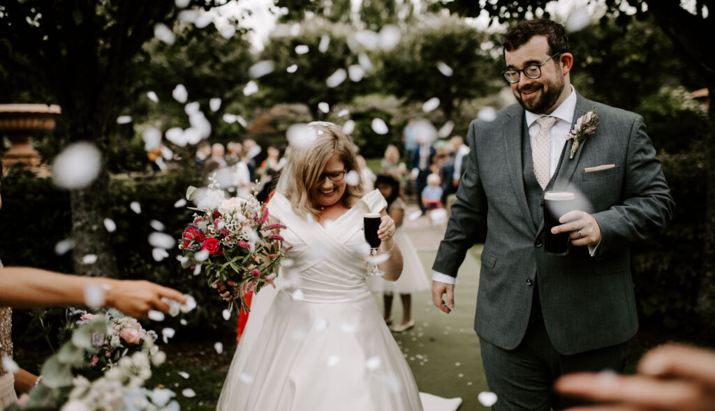 Bride and groom walk down aisle as newlyweds drinking Guinness with confetti thrown in the air